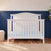 Matte white Child Craft Hampton Arch Top 4-in-1 Convertible Crib with vertical slats and a light blue polka dot mattress sheet.