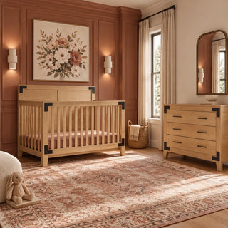 The Child Craft Lucas 2-Piece Nursery Set, featuring a wooden crib and a three-drawer dresser with dark metal corner accents, is placed in a room with mauve paneled walls.