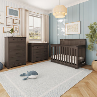 A Child Craft Redmond 4 Piece Nursery Set with Crib, Dresser with Changing Tray and Chest in dark wood, set on a light patterned rug with a whale plush toy.