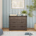 A Dapper Gray Child Craft Redmond 3 Drawer Dresser with one top drawer and two wide lower drawers, topped with a woven basket, a toy sailboat, and a potted plant.