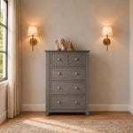 A gray Atwood 4-Drawer Chest, Lunar Gray, featuring a diagonal-slat design on the top drawers, topped with a stuffed toy and a wooden stacking toy.