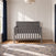 Child Craft Atwood 4-in-1 Convertible Crib in Lunar Gray, featuring a chevron-patterned back panel and vertical slats, positioned in a room with white paneled walls and a patterned area rug.