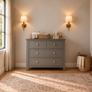 Child Craft Atwood 3-Drawer Dresser, Lunar Gray, with a woven basket of baby essentials and a stuffed bunny on top, positioned between two wall-mounted lamps.