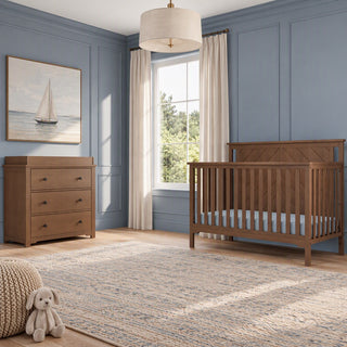 A Child Craft Hampton Flat Top 4-in-1 Convertible Crib in Dusty Heather paired with a matching three-drawer dresser, positioned in a nursery with blue walls and a slatted design.