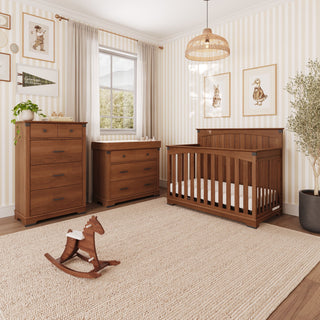 A nursery set from the Child Craft Redmond 4 Drawer Chest, Coach Cherry collection, featuring a tall 4-drawer chest, a changing table, and a crib in a matching dark wood finish, with a wooden rocking horse on the floor.