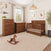 A nursery set from the Child Craft Redmond 4 Drawer Chest, Coach Cherry collection, featuring a tall 4-drawer chest, a changing table, and a crib in a matching dark wood finish, with a wooden rocking horse on the floor.