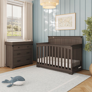 Dark wood Child Craft crib and a matching Dapper Gray Redmond 3 Drawer Dresser in a nursery with light blue walls and a rug.