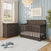 Dark wood Child Craft crib and a matching Dapper Gray Redmond 3 Drawer Dresser in a nursery with light blue walls and a rug.