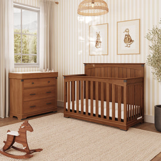 A wooden crib and matching Child Craft Redmond 3 Drawer Dresser in Coach Cherry in a nursery with a rocking horse.