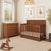 A wooden crib and matching Child Craft Redmond 3 Drawer Dresser in Coach Cherry in a nursery with a rocking horse.