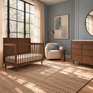 Child Craft Surrey Hill 4-in-1 Convertible Crib in Toasted Chestnut, a wooden crib with slatted sides and a mattress, positioned in a nursery next to a wooden dresser and an armchair.