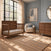 Child Craft Surrey Hill 4-in-1 Convertible Crib in Toasted Chestnut, a wooden crib with slatted sides and a mattress, positioned in a nursery next to a wooden dresser and an armchair.