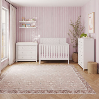 Matte White Child Craft Atwood 4-Drawer Chest in a nursery setting with a matching crib, changing table, and pink patterned wallpaper.
