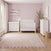 Matte White Child Craft Atwood 4-Drawer Chest in a nursery setting with a matching crib, changing table, and pink patterned wallpaper.