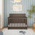 A dark wood Child Craft Redmond 4 Piece Nursery Set convertible crib with slats stands against a light blue paneled wall as the centerpiece of the room.