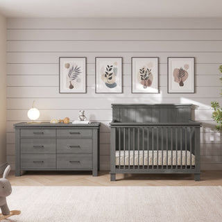 A dark gray Child Craft Denman Double Dresser, Midnight Gray with six drawers stands next to a matching dark gray crib in a nursery.
