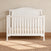 Hampton Arch Top 4-in-1 Convertible Crib in matte white wood with an arched headboard, slatted sides, and a beige gingham-patterned mattress.