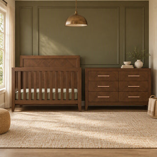 A toasted chestnut Child Craft Kieran 6-Drawer Double Dresser positioned next to a matching wooden crib in a nursery.