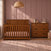 A Child Craft crib and matching Redmond 3 Drawer Dresser in Coach Cherry sit on a patterned rug in a room with paneled walls.