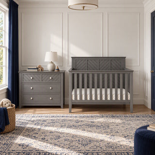 A gray Child Craft Atwood 3-Drawer Dresser, Lunar Gray with diamond-patterned drawer fronts next to a matching crib in a nursery.