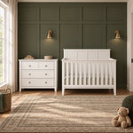A white Child Craft Atwood 3-Drawer Dresser, Matte White sits next to a matching white slatted crib in a nursery.