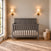 Child Craft Atwood 4-in-1 Convertible Crib in Lunar Gray, featuring a diagonal slat design on the headboard, positioned against a wall between two wall-mounted lamps.