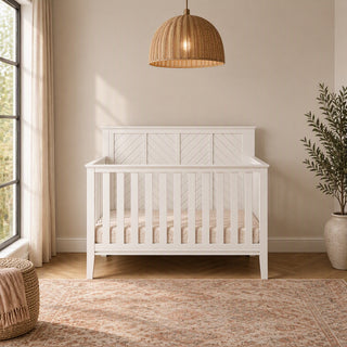A matte white Atwood 4-in-1 Convertible Crib featuring a chevron-patterned headboard.