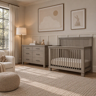 A gray Child Craft Denman Double Dresser, Crescent Gray with six drawers standing next to a matching crib in a nursery.