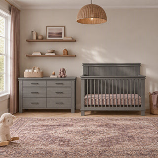 A gray wooden Denman Double Dresser, Midnight Gray, with six drawers stands next to a matching crib.