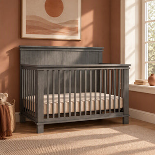 A gray, rectangular Child Craft Denman 4-in-1 Convertible Crib in Midnight Gray with a rectangular headboard.