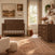 A Child Craft Kieran 6-Drawer Double Dresser in Toasted Chestnut with copper-toned pulls, positioned in a room with a matching crib, patterned area rug, and wall-mounted shelving.