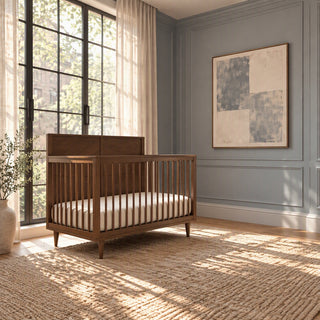 Child Craft Surrey Hill 4-in-1 Convertible Crib in toasted chestnut with a paneled headboard, set on a textured rug in a nursery with a large window and gray walls.