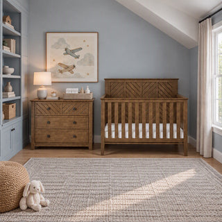 A Child Craft Atwood 3-Drawer Dresser in Cocoa Bean and a crib with a matching wood chevron pattern, displayed in a nursery setting with a rug and wall decor.