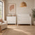 A white Child Craft Atwood 3-Drawer Dresser, Matte White with a changing table topper and a matching white slatted crib in a nursery, with a woven pendant light hanging above.