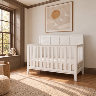 Matte white Atwood 4-in-1 Convertible Crib with a paneled headboard featuring diagonal trim and baby-safe finishes.