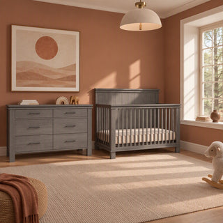 A gray wooden Denman Double Dresser, Midnight Gray with six drawers and a matching slatted crib in a room with terracotta walls.