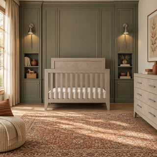 Gray wood crib in a nursery with a paneled accent wall, flanked by built-in shelving, wall sconces, and a Child Craft Kieran 6-Drawer Double Dresser, Crescent Gray.