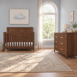 A wooden crib and a matching Child Craft Kieran 6-Drawer Double Dresser, Toasted Chestnut with six drawers and copper-colored handles in a nursery.