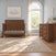 A wooden crib and a matching Child Craft Kieran 6-Drawer Double Dresser, Toasted Chestnut with six drawers and copper-colored handles in a nursery.