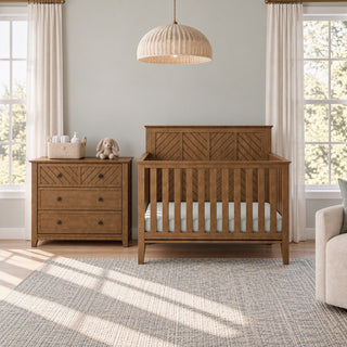 A wooden baby crib and matching Child Craft Atwood 3-Drawer Dresser, Cocoa Bean in a nursery with light-colored walls and windows.