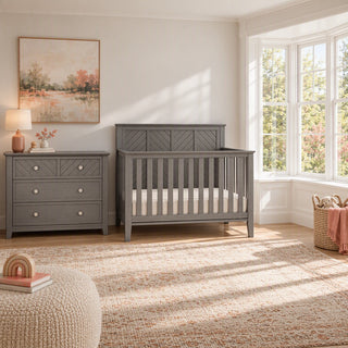 A gray Atwood 3-Drawer Dresser, Lunar Gray sits next to a matching gray slatted crib in a nursery.
