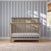 Child Craft Denman 4-in-1 Convertible Crib in Crescent Gray with slatted sides set against a blue and white striped wallpapered wall.