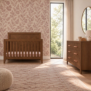 Child Craft Kieran 6-Drawer Double Dresser, Toasted Chestnut with six drawers and horizontal metal pulls, positioned next to a matching wooden crib in a nursery.
