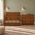 A wooden baby crib and matching Child Craft Redmond 3 Drawer Dresser in Coach Cherry in a nursery.