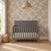 Child Craft Atwood 4-in-1 Convertible Crib in Lunar Gray, featuring a slat design and a patterned mattress against a floral wallpapered wall.