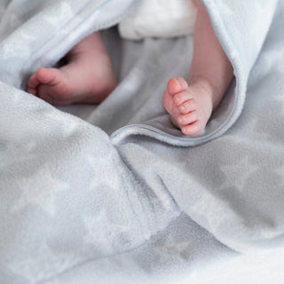 Close-up of a babys feet peeping out from under a cozy HALO Swaddle Micro-Fleece TOG 3.0 with star patterns. The adjustable wings offer comfort and support healthy hip development, keeping the toes snugly wrapped in warmth.