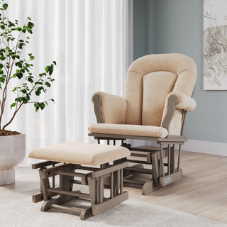 A beige cushioned glider chair with matching ottoman sits on a wooden floor near a potted plant, white curtains, and abstract wall art in a cozy, sunlit room—perfectly complementing your Child Craft Hampton Flat Top 3 Piece Nursery Set with Crib, Dresser and Glider, featuring baby-safe finishes.