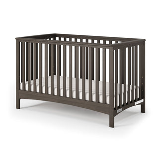 The Child Craft London 4-in-1 Convertible Crib in Dapper Gray features vertical slats on all sides, a simple modern design, and comes with a white mattress inside.