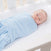 A baby peacefully sleeps wrapped in a HALO Swaddle Micro-Fleece TOG 3.0 in a crib. The adjustable wings ensure comfort and promote healthy hip development. The baby, surrounded by white bars and light-colored bedding, rests on their back with eyes closed.