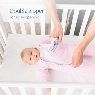A baby lies in a crib wearing Baby Merlins Magic Sleepsuit® 100% Cotton by HALO, while an adult opens the double zipper on the sleepsuit. Text reads: Double zipper for easy opening.